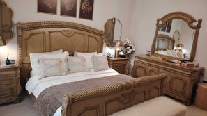 A classic bedroom with a large bed, ornate wooden headboard, matching nightstands, and a dresser with a mirror. - Sleeps 8 people! Apartment 5 minutes to Abdoun w balcony a in Dair Ghbar!  (Amman)
