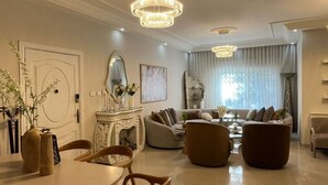 A modern living room with a fireplace, sofas, a dining table, and a chandelier.