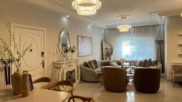 A modern living room with a fireplace, sofas, a dining table, and a chandelier. - Sleeps 8 people! Apartment 5 minutes to Abdoun w balcony a in Dair Ghbar!  (Amman)