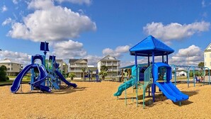 Un parc infantil amb tobogans blaus i elements per escalar, envoltat d'edificis residencials.