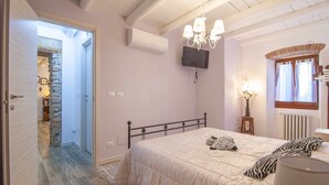 Un dormitorio con una cama, un candelabro, un televisor y una ventana con cortinas.