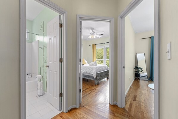 A hallway leading to a bedroom with a bed, a ceiling fan, and a window.