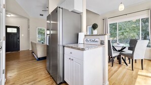 Een moderne keuken met witte kasten, een roestvrijstalen koelkast, een granieten aanrechtblad en een eethoek met een tafel en stoelen.