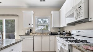 Een keuken met witte kastjes, een granieten aanrechtblad, een ingebouwde magnetron, een gasfornuis en een raam met jaloezieën.