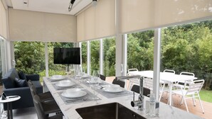 A modern dining area with a long table, white chairs, and a large window overlooking a garden. - Garden Pod @ Gardens by the Bay (Singapore)