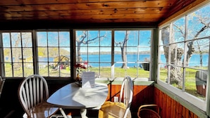 Una cabaña de madera con comedor, que incluye una mesa y sillas, y ventanas amplias con vista a un lago y barcos amarrados.