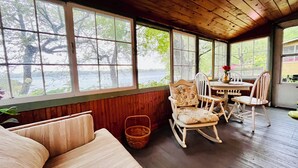 Una habitación acogedora con techo de madera, ventanas amplias con vistas a un lago, una mesa de comedor con sillas y un banco acolchado.