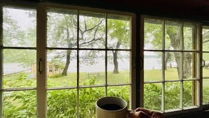 Una habitación con un ventanal grande que da a un área verde con árboles y una masa de agua.