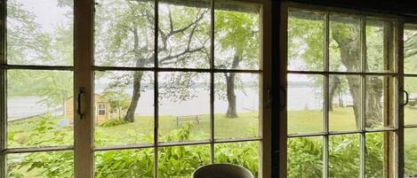 A room with a large window overlooking a grassy area with trees and a body of water.