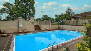 Ein rechteckiger Swimmingpool mit glasklar blauem Wasser, umgeben von einer Betonplattform. Liegestühle und eine Treppe, die zu einer erhöhten Ebene führen.