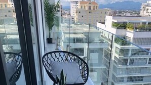 Un balcón con dos sillas de mimbre negro, una con cojín blanco y una pequeña planta en maceta.