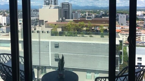 Un balcón con vista a un paisaje urbano, que incluye edificios y montañas al fondo.