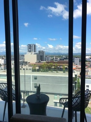 A balcony with a view of a cityscape, including buildings and mountains in the distance.