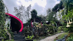 A pathway leading to a building with a distinctive red archway, surrounded by lush greenery and a stone staircase.