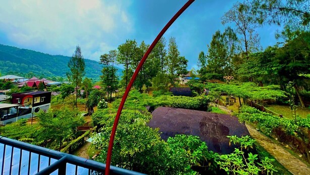 A lush landscape with a large rock, trees, and a distant view of a village.