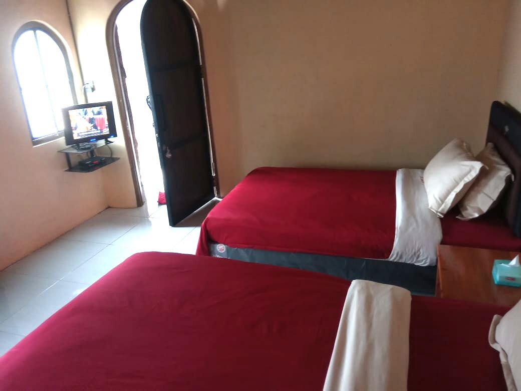 A hotel room with two red beds, a television on a stand, and a door leading to another room.