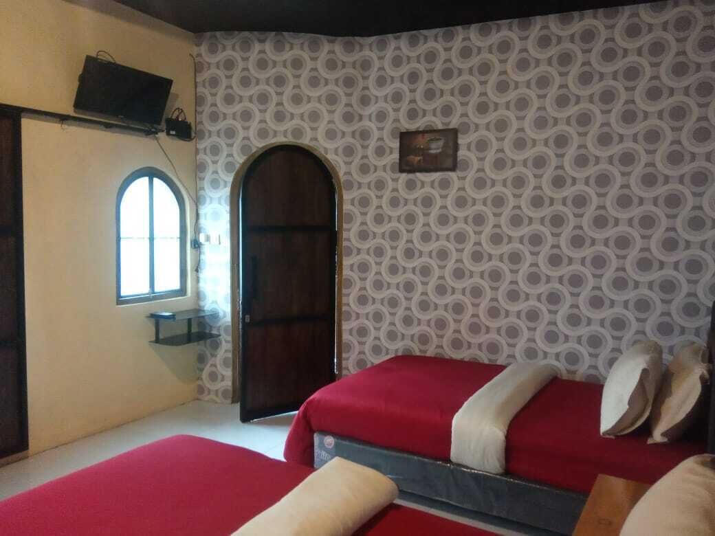 A bedroom with two beds, a window, a door, and patterned wallpaper.