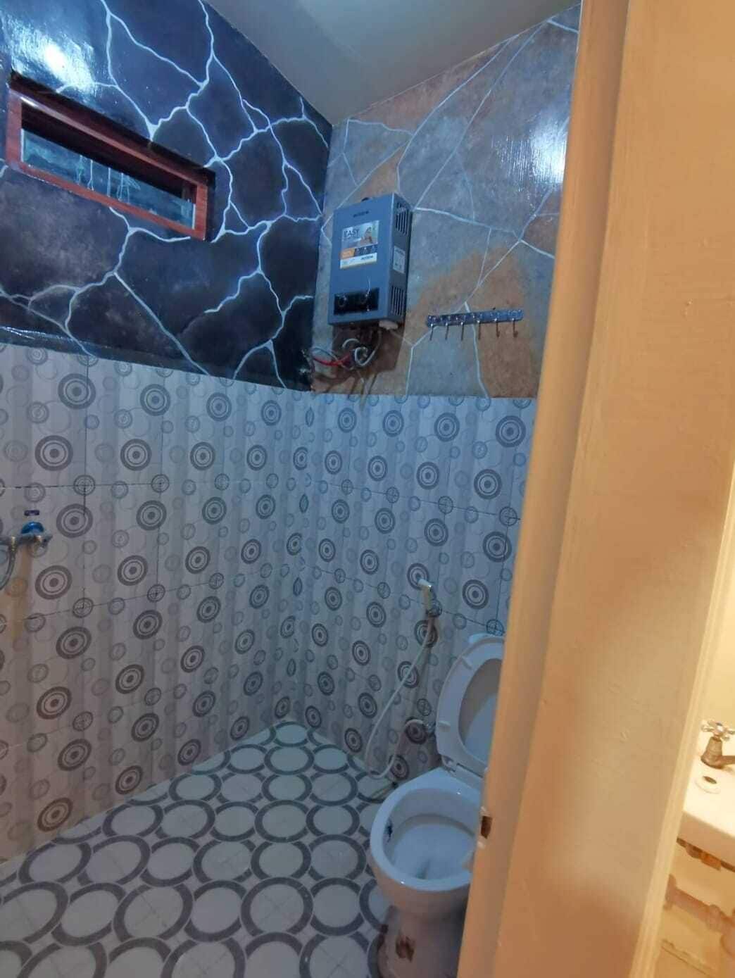A bathroom with a patterned floor, a toilet, a shower area, and a wall-mounted heater.