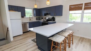Eine moderne Küche mit dunkelblauen Schränken, einem weißen Kühlschrank, Edelstahlgeräten und einer großen Kochinsel mit Barhocker.
