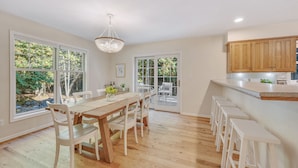 A spacious kitchen with a wooden dining table, white chairs, and a large window offering a view of greenery. - Hot Tub, Family Friendly + 2 King Beds, Game Room, Secluded -Close to SB & Beach (Ellison Bay)