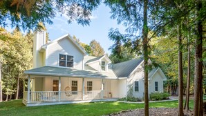 A two-story house with a porch, surrounded by trees and a well-maintained lawn. - Hot Tub, Family Friendly + 2 King Beds, Game Room, Secluded -Close to SB & Beach (Ellison Bay)