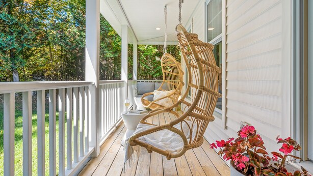 A porch with a wicker swing chair, a white table, and a potted plant. - Hot Tub, Family Friendly + 2 King Beds, Game Room, Secluded -Close to SB & Beach (Ellison Bay)