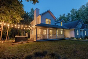 A two-story house with a covered porch, a hot tub, and string lights.