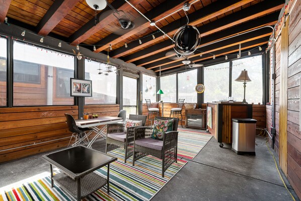 A rustic interior with wooden beams, large windows, wicker furniture, and a striped rug. - Hippie Pickle - Charming, eclectic home near everything in Wimberley + Hot tub! (Wimbereley)