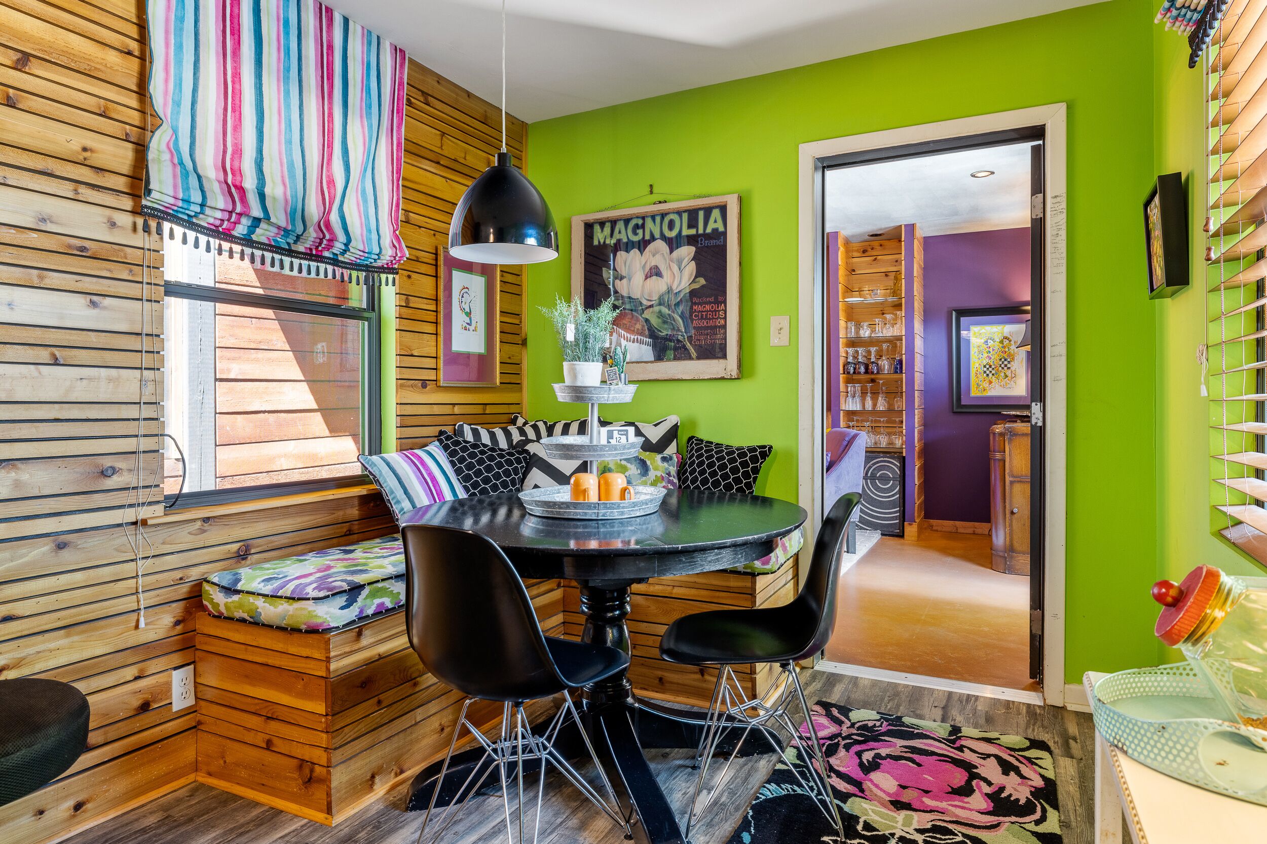 Un coin repas avec un mur en bois, un mur d’accent de couleur verte, une table avec des chaises et une fenêtre avec des rideaux.