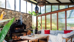 A cozy outdoor seating area with a stone wall, a wood-burning stove, and a view of the outdoors. - Reserve-front to two beaches with hot tub & fire (Bowentown)