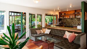 A modern living room with a glass coffee table, a sofa, and a kitchen area with a checkered backsplash. - Reserve-front to two beaches with hot tub & fire (Bowentown)