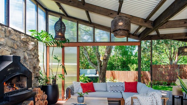 An outdoor living area with a stone wall, a wood-burning stove, a sofa with cushions, a coffee table, and hanging lights. - Reserve-front to two beaches with hot tub & fire (Bowentown)