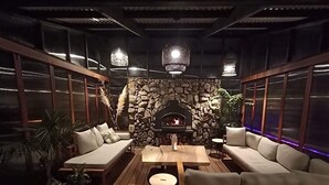A cozy lounge area with a stone fireplace, cushioned seating, and hanging lights. - Reserve-front to two beaches with hot tub & fire (Bowentown)