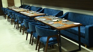 Een vergaderzaal met lange tafels, blauwe fauteuils en een grote blauwe bank.