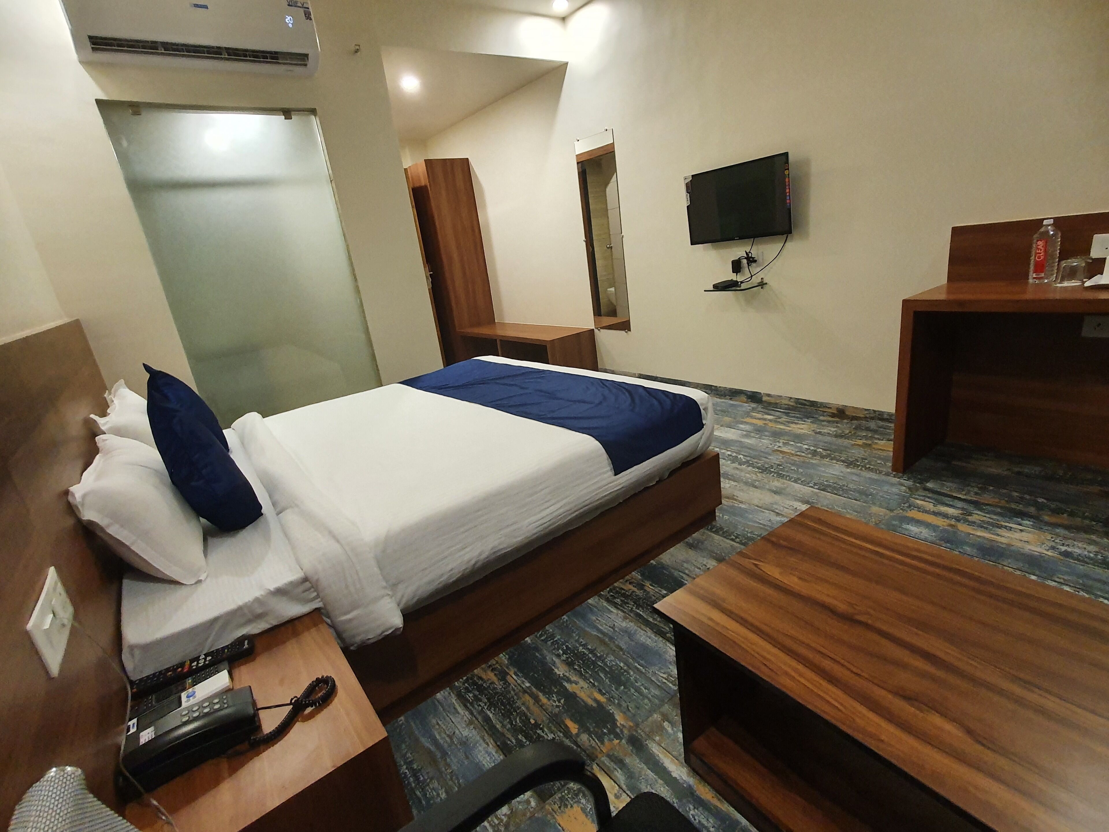 A hotel room with a bed, bedside tables, a desk, a TV, and a water bottle.