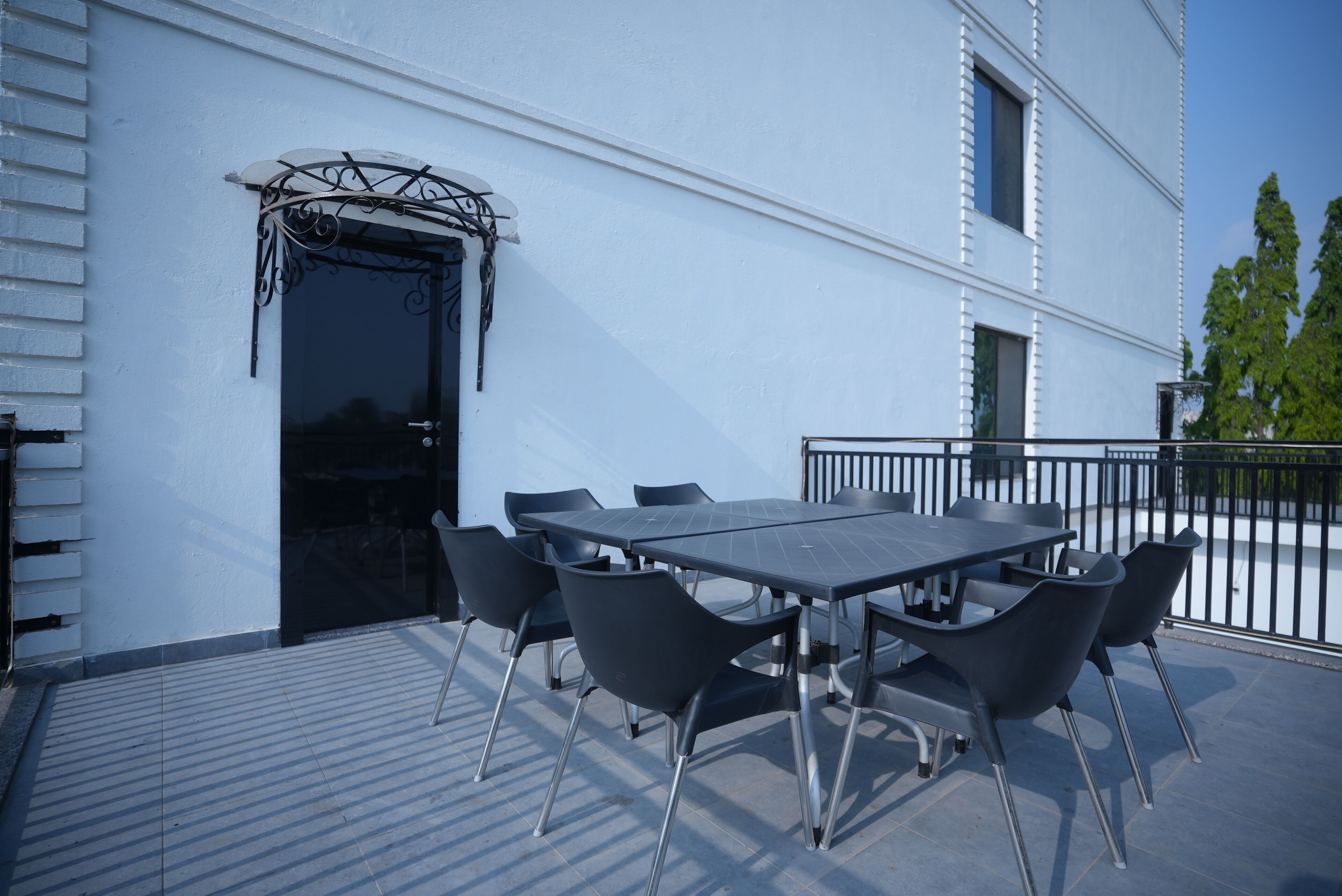 An outdoor patio with a table and chairs, a black door, and a white building facade.