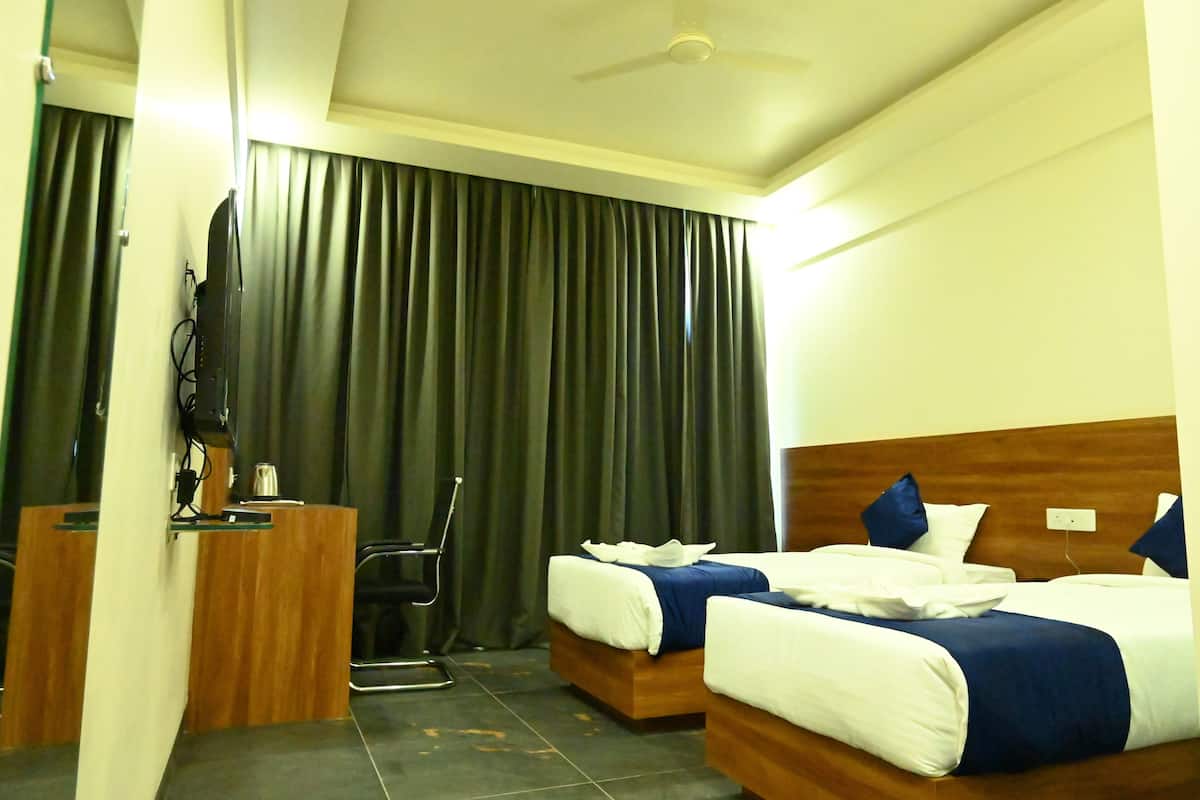 A hotel room with two beds, a desk, a television, and a ceiling fan.