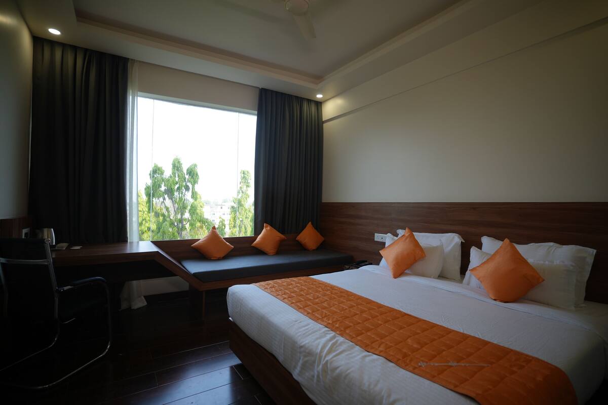A hotel room with a bed, a desk, and a window with curtains.