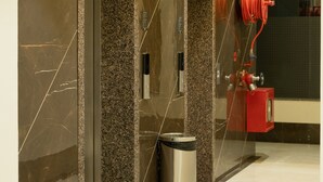 Een moderne lift met een metalen afwerking, een prullenbak en een rode brandslang aan de muur.