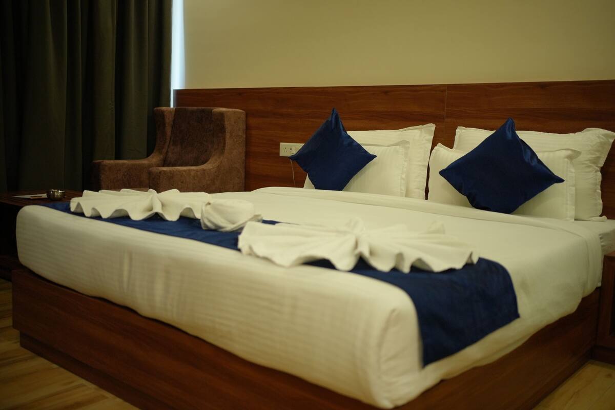 A neatly made bed with white and blue bedding, a wooden headboard, and a brown armchair beside it.