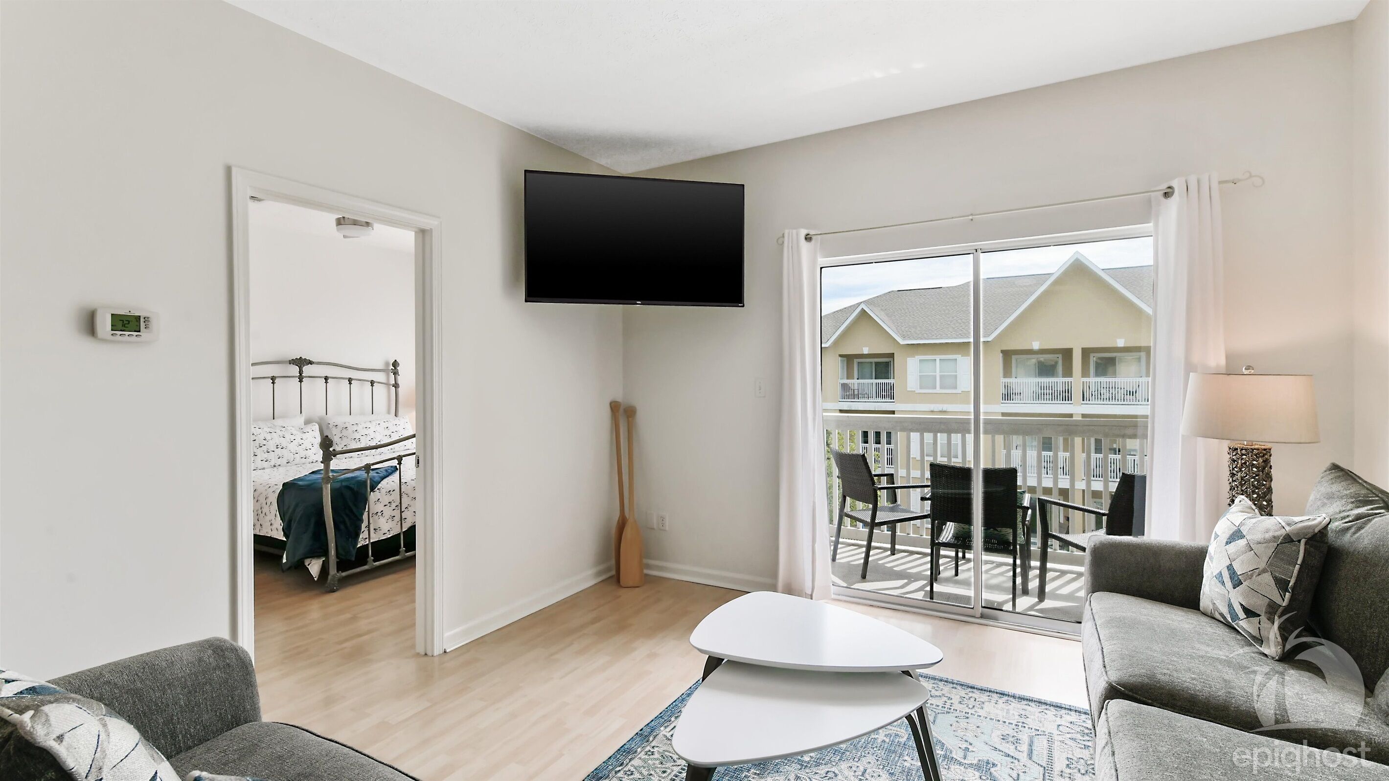A modern living room with a flat-screen TV, a sofa, a coffee table, and a balcony with outdoor furniture.