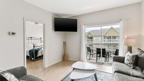 A modern living room with a flat-screen TV, a sofa, a coffee table, and a balcony with outdoor furniture.