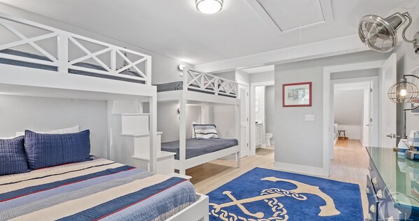 A bedroom with bunk beds, a bed with a striped bedspread, a blue rug with a nautical anchor design, and a glass cabinet with a light fixture. - VillaParadiso-Sandestin 3BR/3BA:Cart to the Beach! (Miramar Beach)
