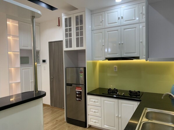 A modern kitchen with white cabinets, a stainless steel refrigerator, and a black countertop. - Saigon South Residence - Vina We Stay (Ho Chi Minh City)