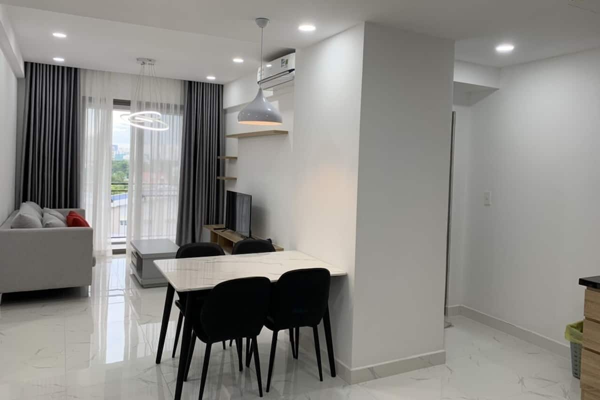A modern living room with a sofa, a dining table with chairs, and a large window with curtains.