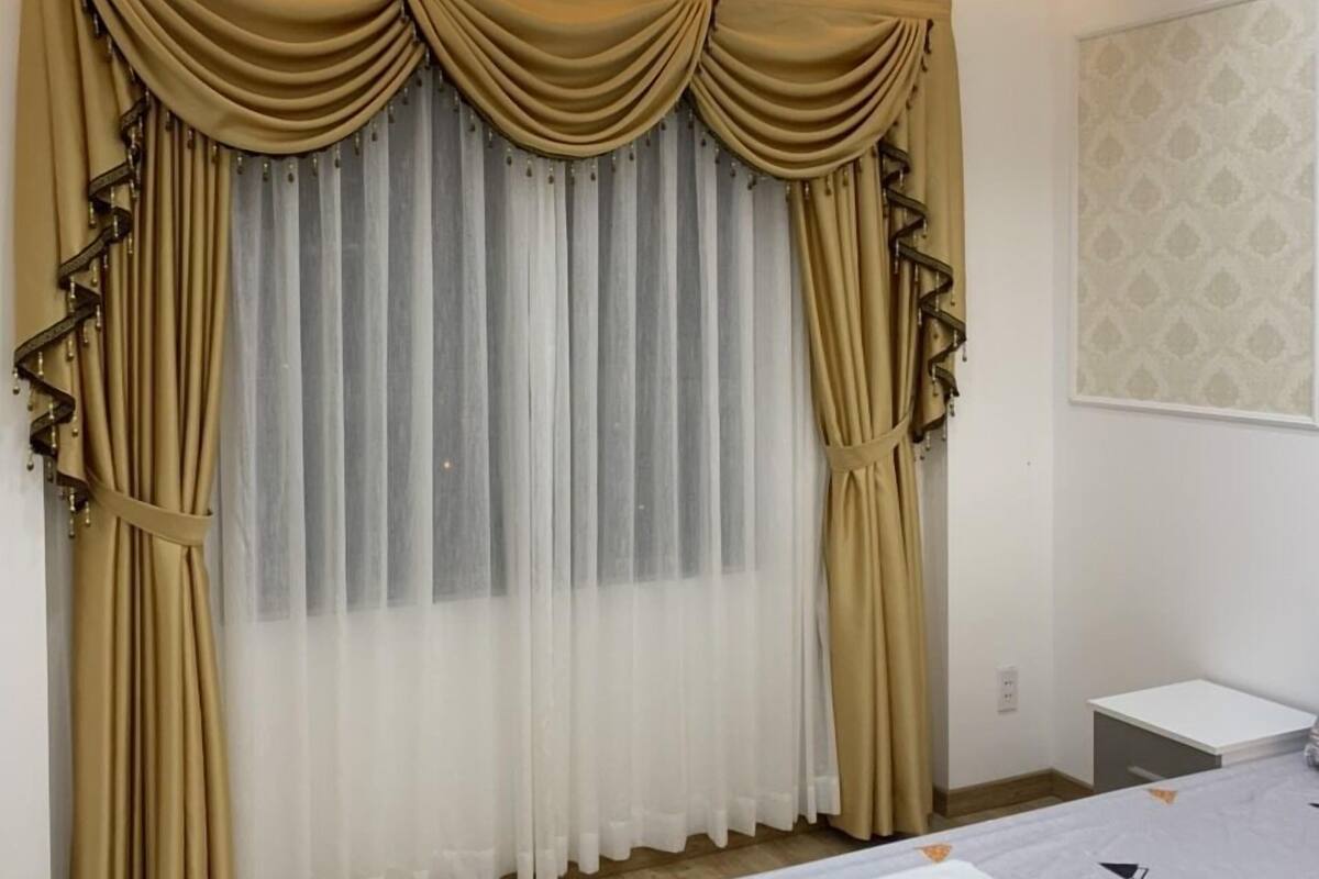 A bedroom with a bed, a nightstand, and a window with beige curtains.