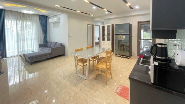 Una sala de estar moderna con una mesa de comedor de vidrio, un sofá y una zona de cocina con una cafetera.