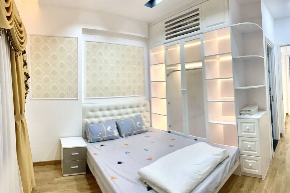 A bedroom with a bed, bedside tables, a wardrobe with lighting, and a bathroom visible through an open door.