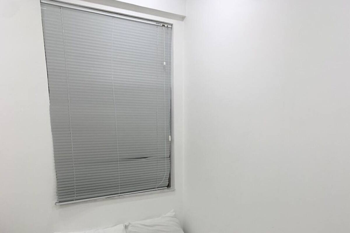 A single-bed room with a window, a bedside table, and a quilted bedspread.