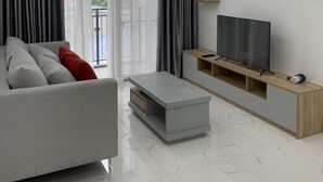 Una sala de estar moderna con un sofá gris, una mesa de centro, un televisor sobre un mueble de madera y una lámpara de techo.